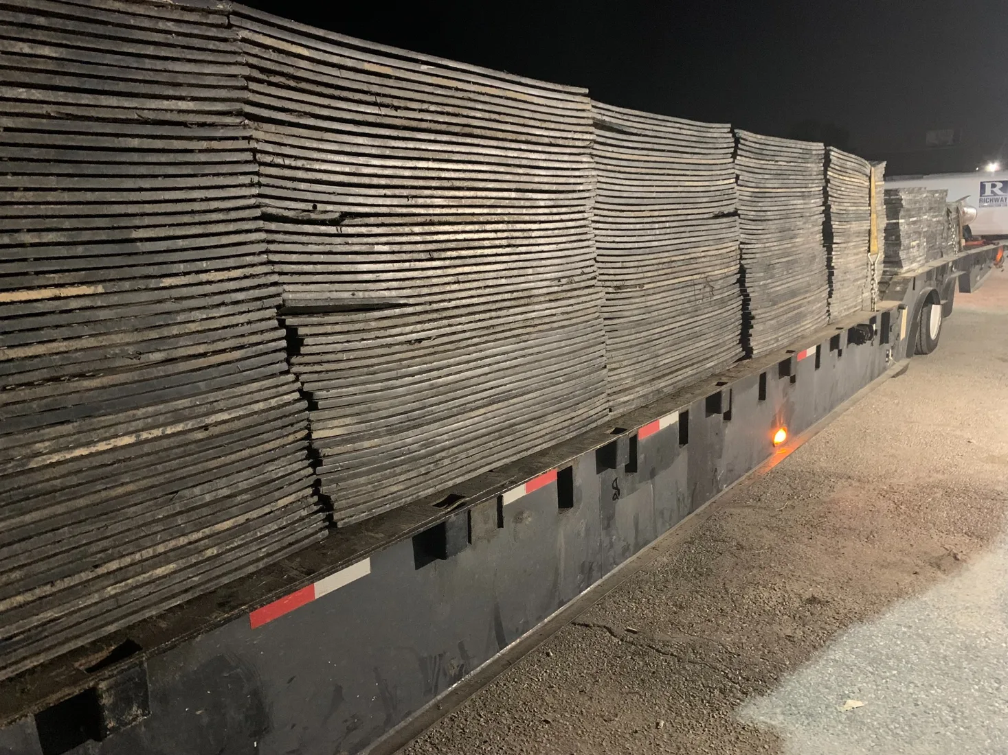Large shipment of Trak Mat ground protection panels loaded on a flatbed trailer at night